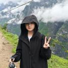 Person wearing a black hoodie and holding a water bottle, with mountains and clouds in the background.